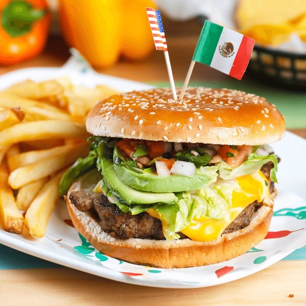 A burger with avocado, cheese, lettuce, and pico de gallo, served with fries.