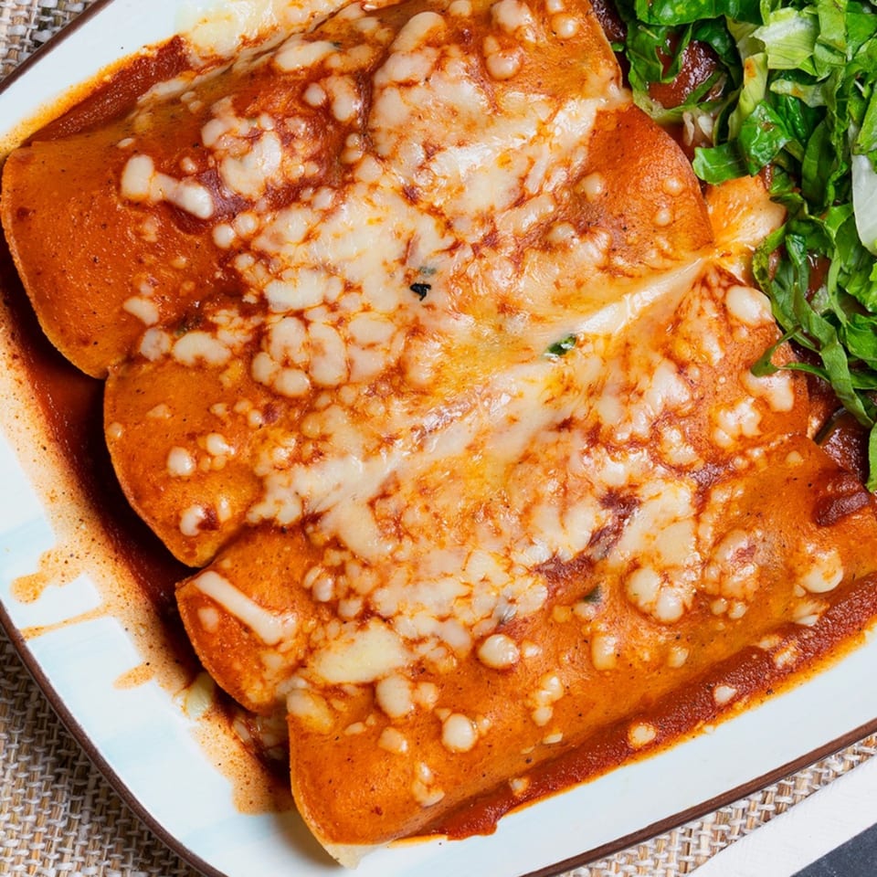Three cheesy enchiladas covered in red sauce, served with a side of green shredded lettuce.