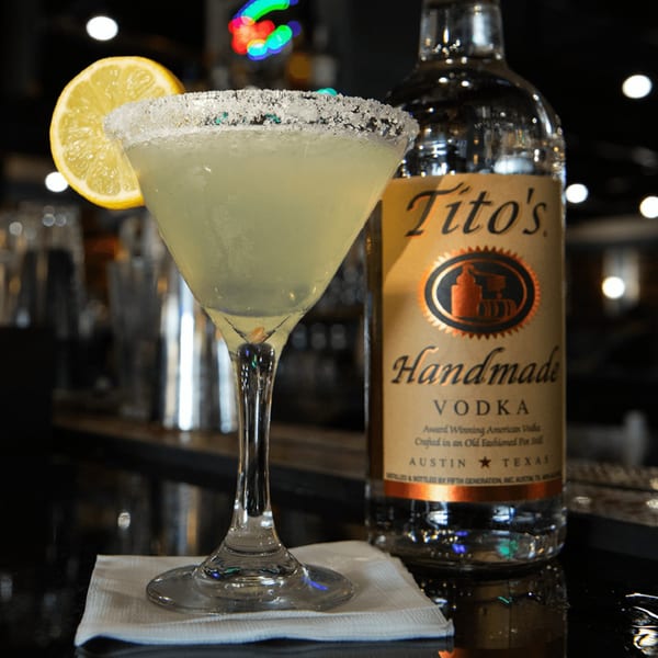 A Tito's Handmade Vodka cocktail with a lemon slice and sugar rim next to a bottle of Tito's.