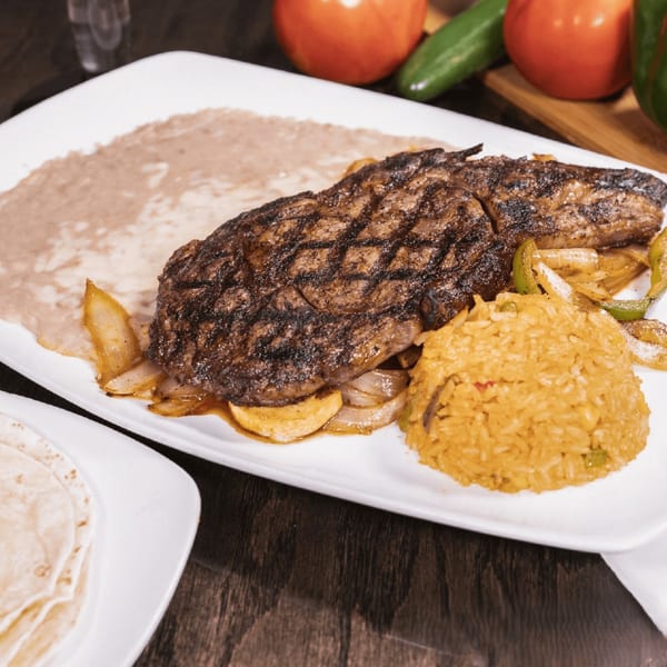 Grilled steak with onions and peppers, yellow rice, and refried beans on a white plate.