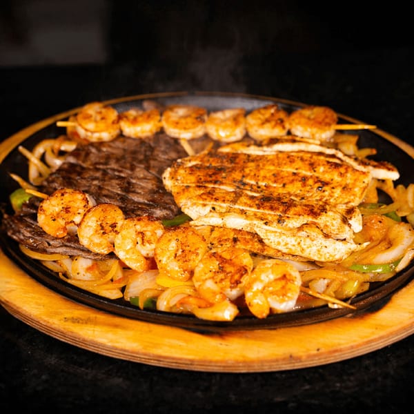 Sizzling fajita platter with steak, chicken, and shrimp skewers, served over onions and peppers.