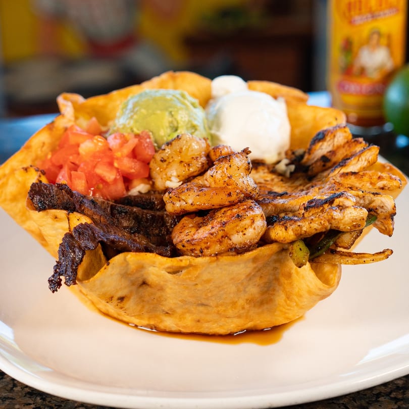 A large taco salad with steak, shrimp, chicken, guacamole, sour cream, and diced tomatoes.