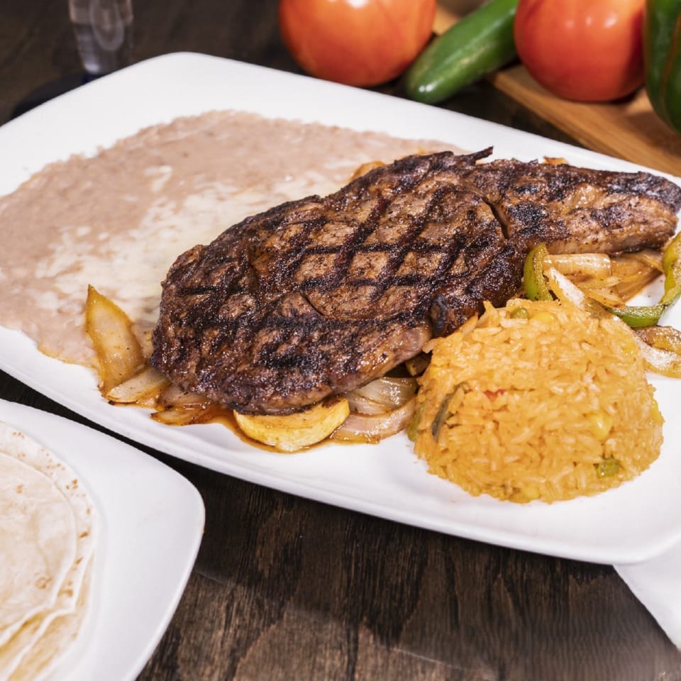 Grilled steak with onions, peppers, rice, refried beans, and tortillas on a white plate.