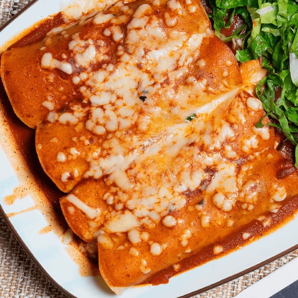 Three cheesy enchiladas covered in red sauce, served with a side of fresh green lettuce.
