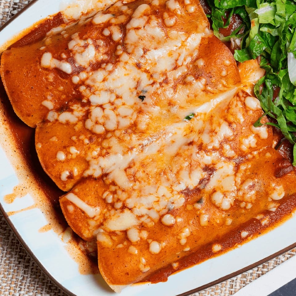 Three cheesy enchiladas covered in red sauce, served with a side of fresh green lettuce.