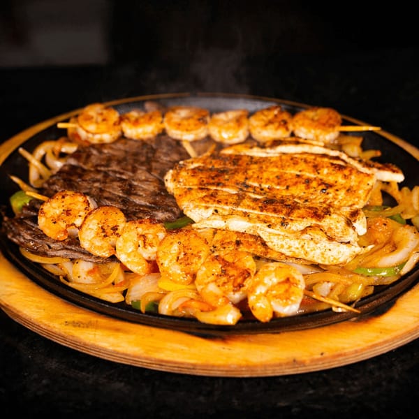 Sizzling fajitas with steak, chicken, and shrimp skewers, served with onions and peppers.