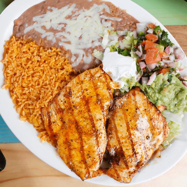 Grilled chicken with rice, refried beans, guacamole, pico de gallo, and sour cream on a white plate.