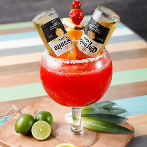 Two Coronita beers inverted into a large, red, salt-rimmed margarita glass with limes and fruit.