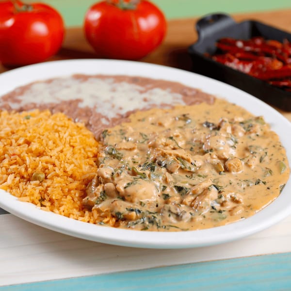 A plate of Mexican food with rice, refried beans, and chicken in a creamy sauce.