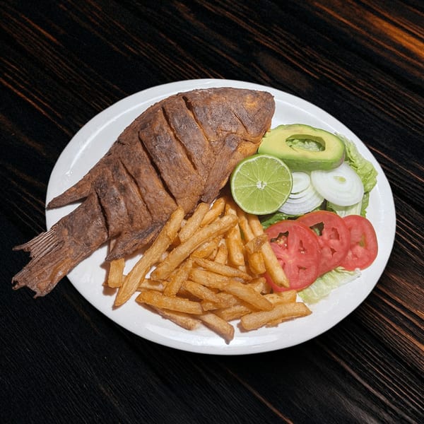 Fried whole fish with french fries, a lime wedge, avocado, and a side salad.