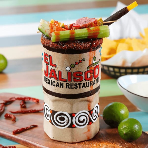 A large, garnished michelada from El Jalisco Mexican Restaurant, with limes and chili peppers nearby.